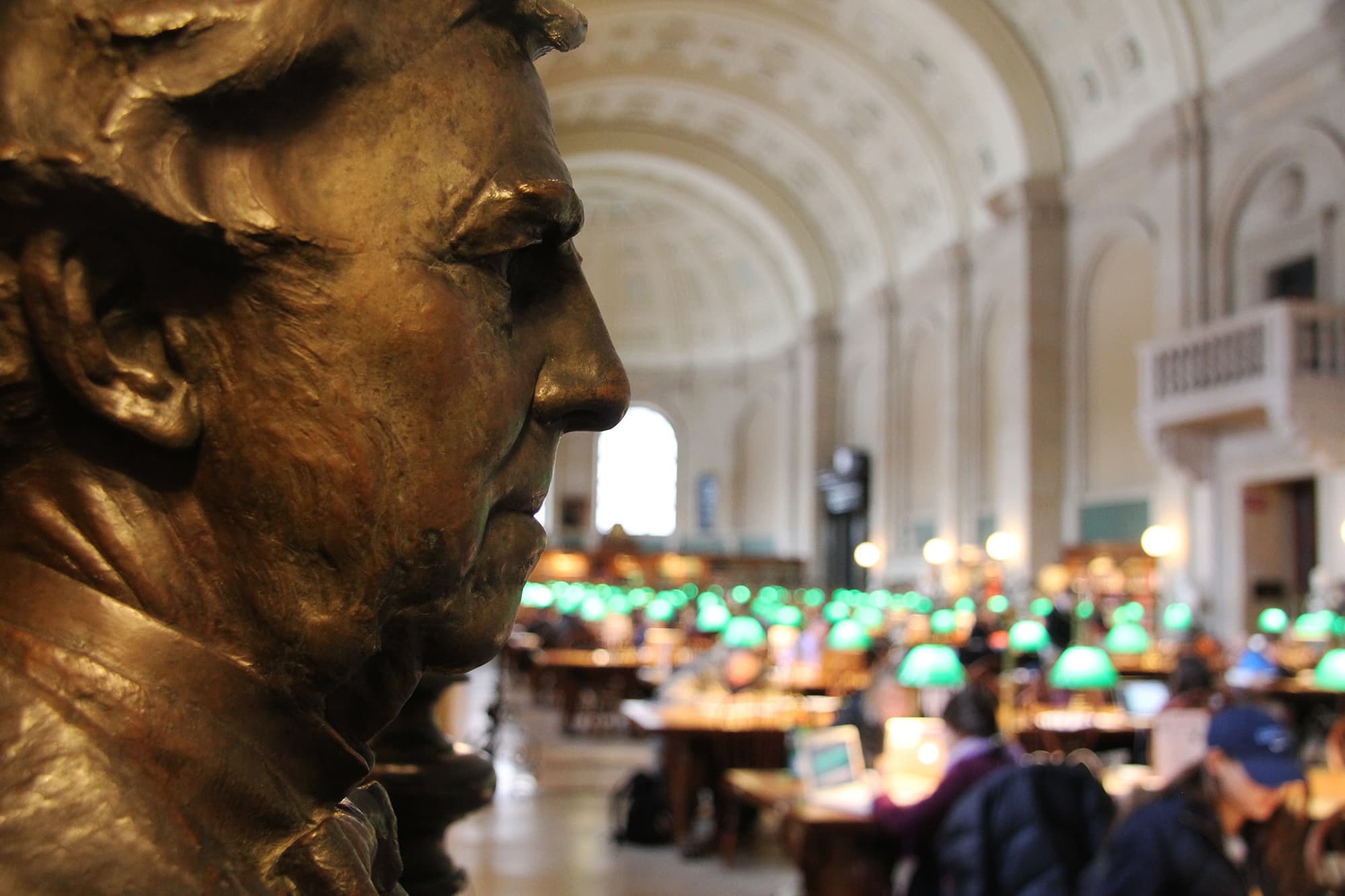 Close-up of a statue in a historic library setting with blurred background.