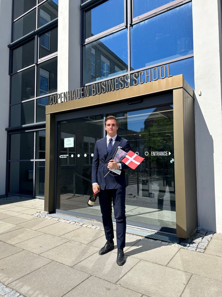 Tomasz Felpel celebrating graduation at Copenhagen Business School in Denmark, holding a Danish flag and champagne.